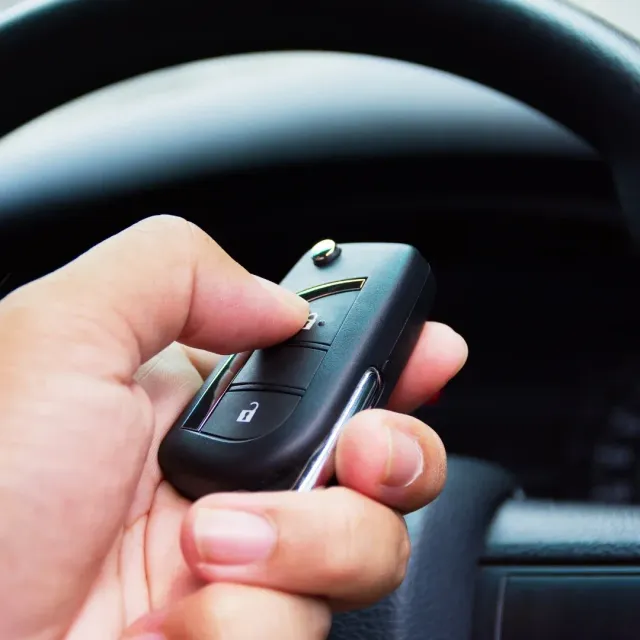 Hand holding a black car key fob in front of a steering wheel Hand holding a black car key fob in front of a steering wheel