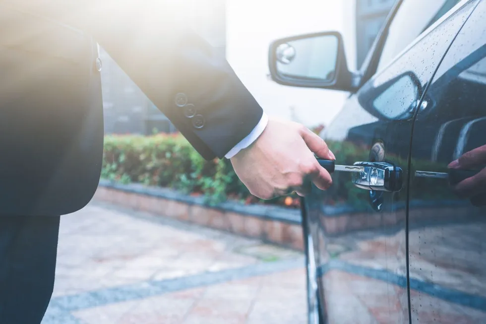 A man in a suit is opening the door of a car.