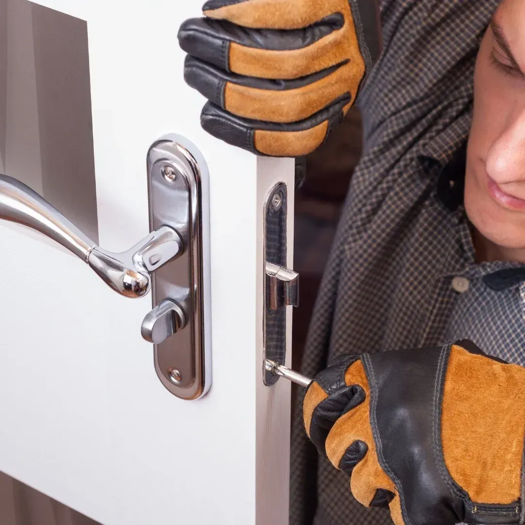 Gloved hands installing a silver door lock on a white door