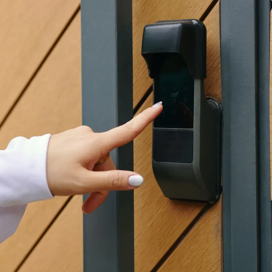 Finger pressing a black wall-mounted keypad on a wooden doorframe